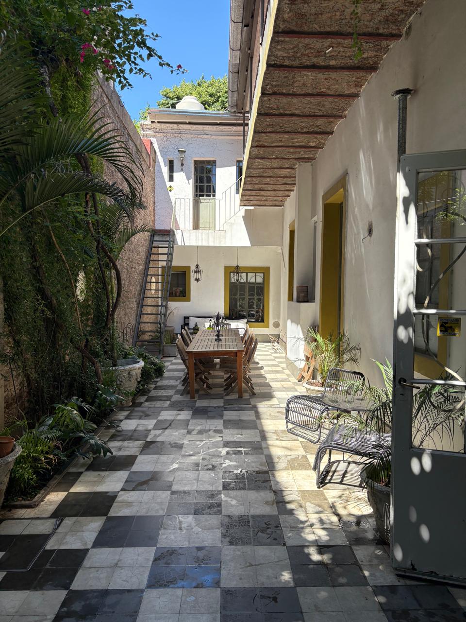 Patio principal visto entre vegetación y mobiliario de la casa